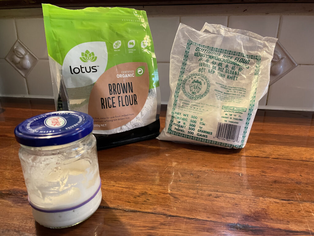 a jar with sourdough starter and in the background is a bag of brown rice flour and a bag of glutinous rice flour