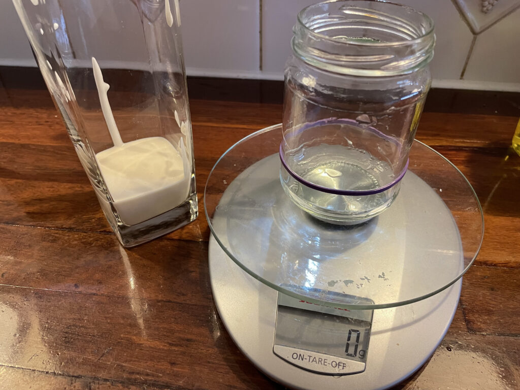 An empty glass jar on a scales with sourdough starter in a nearby glass