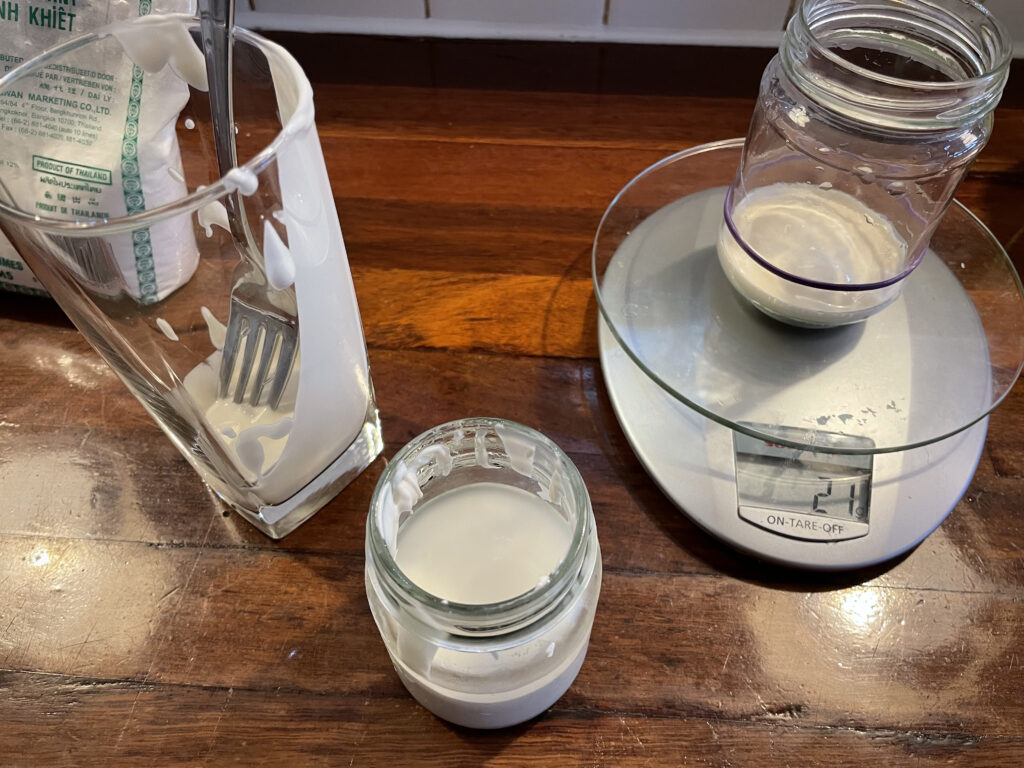 21 grams of sourdough starter measured into the glass jar with the remaining starter in a nearby glass and another glass container nearby with discard
