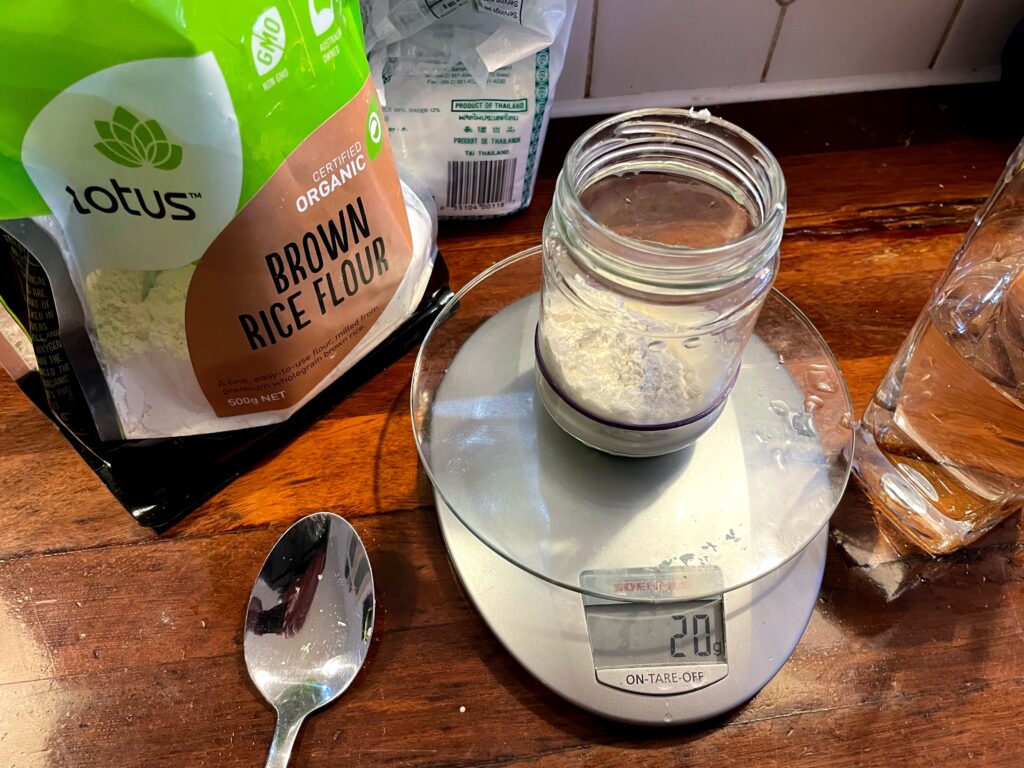 20 grams of flour measured into the glass jar with the bags of flour in the background